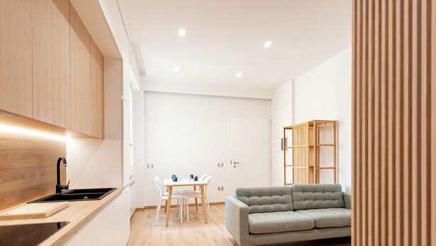 Une cuisine moderne dotée d’une cuisinière intégrée, un coin repas avec une table et des chaises, et un canapé gris dans l’espace salon.