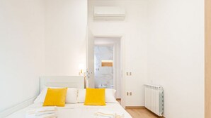 Une chambre à coucher comprenant un lit, deux oreillers, une table de chevet, un radiateur et une porte donnant sur une autre pièce.