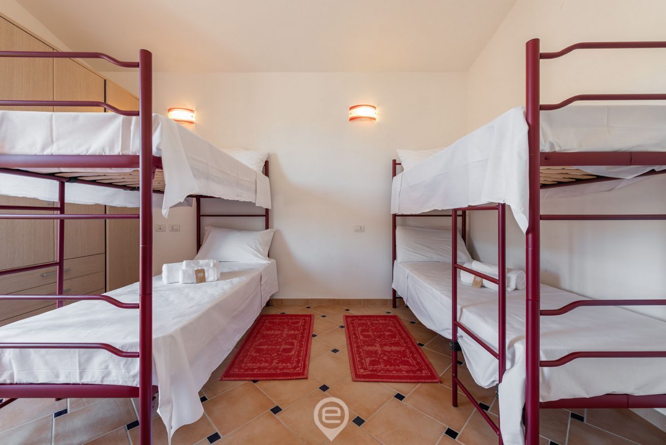 A room with bunk beds, two wall-mounted light fixtures, and red rugs.