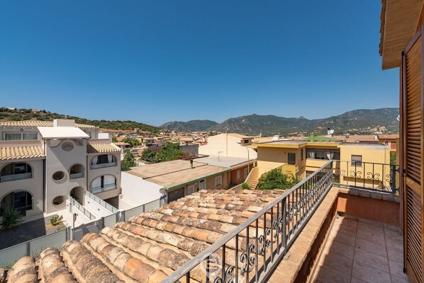 A residential area with terracotta-tiled roofs, a balcony with a metal railing, and a clear view of the surrounding neighborhood and hills in the distance.
