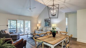 Un vaste espace de vie comprenant une table à manger en bois, des sièges confortables et un ventilateur de plafond.