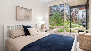 Un dormitorio con una cama grande, una mesita de noche, una lámpara y una ventana que ofrece vistas a árboles y un vehículo en el exterior.