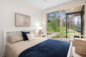 Un dormitorio con una cama grande, una mesita de noche, una lámpara y una ventana que ofrece vistas a árboles y un vehículo en el exterior.