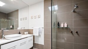 Un baño moderno con ducha envuelta en vidrio, un lavamanos blanco y un espejo sobre él.