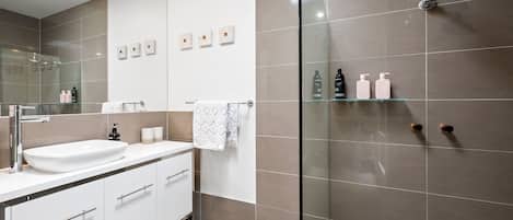 Un baño moderno con ducha envuelta en vidrio, un lavamanos blanco y un espejo sobre él.