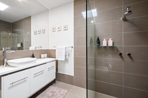 Un baño moderno con ducha envuelta en vidrio, un lavamanos blanco y un espejo sobre él.