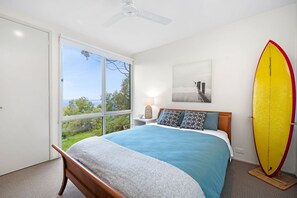A bedroom with a bed, a ceiling fan, a large window, and a surfboard. - Big Hill Retreat (Lorne)