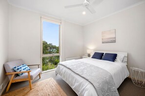 Une chambre à coucher avec un grand lit, une chaise, une table de chevet, une lampe et un ventilateur de plafond.