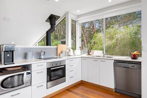 A modern kitchen with white cabinetry, a built-in oven, a dishwasher, and a coffee machine.
