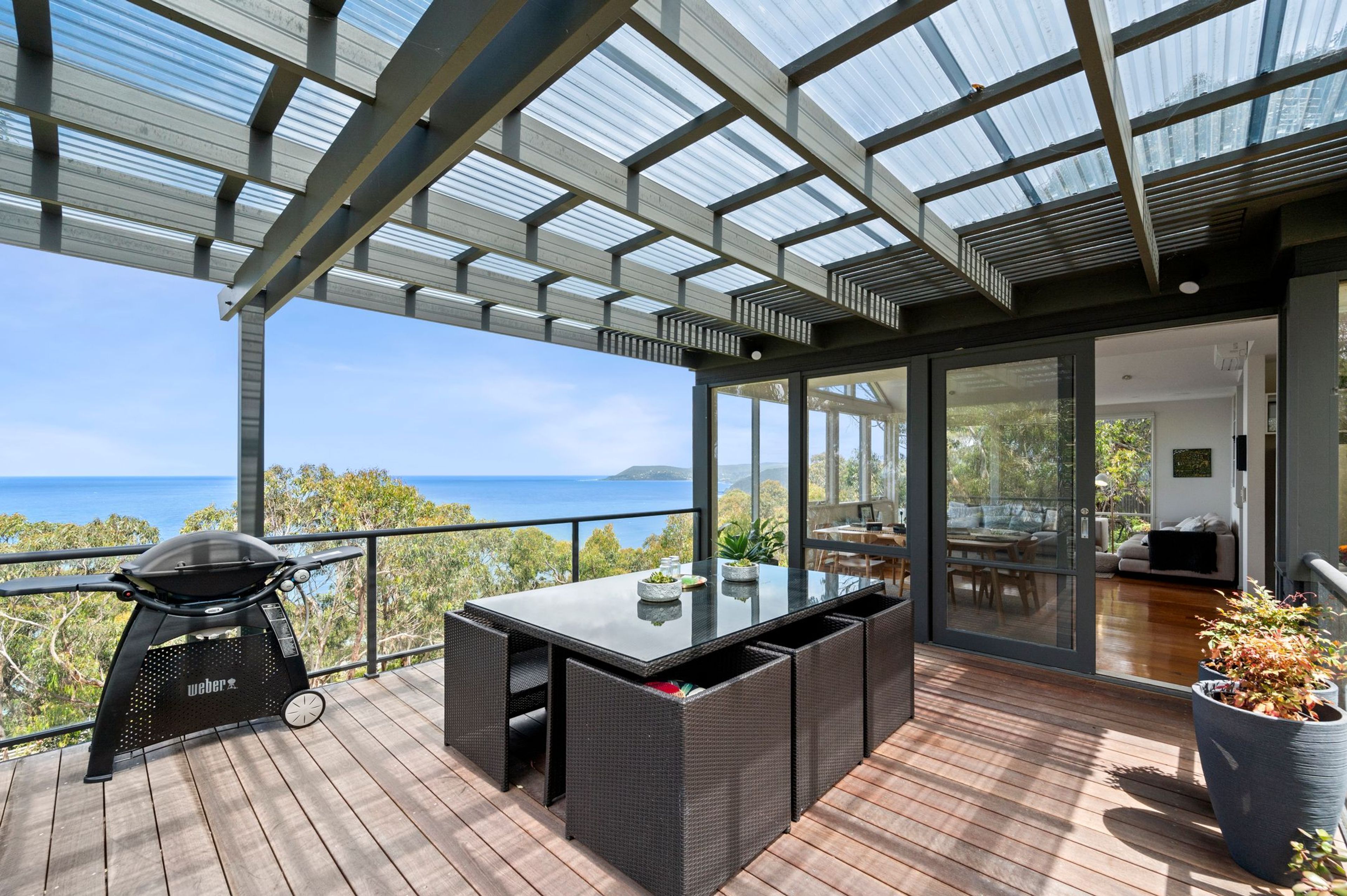 A covered outdoor area with a grill, dining table, and chairs, overlooking a scenic view.