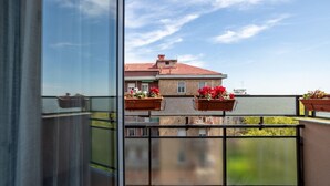 Un balcón con vistas a un edificio de techo rojo, barandilla metálica y macetas con plantas.