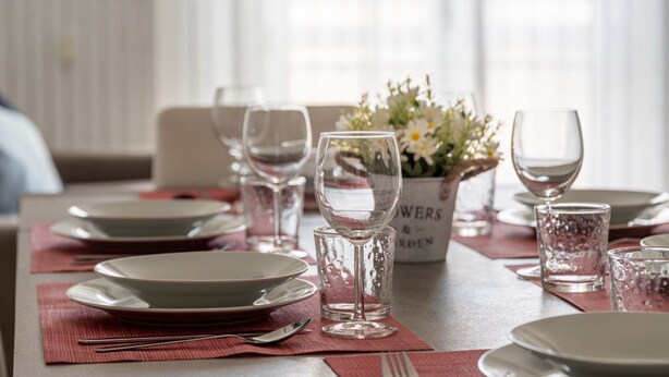 Una mesa de comedor dispuesta con platos, vasos y un florero con flores.