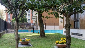Un patio con piscina, dos macetas grandes y un edificio de diseño moderno al fondo.