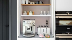 Una cocina con cafetera, tostadora y estantes con tazas y frascos.