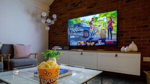 Una sala de estar con pared de ladrillo, un televisor de pantalla plana montado en ella, un balde de palomitas de maíz y un sofá.