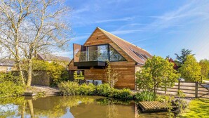 Una casa moderna con un amplio ventanal, fachada de madera y un estanque al frente.