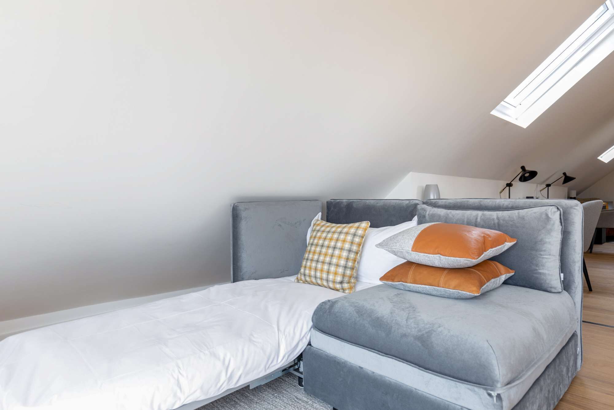 A modern loft bedroom with a grey sofa bed, a white mattress, and a checkered pillow.