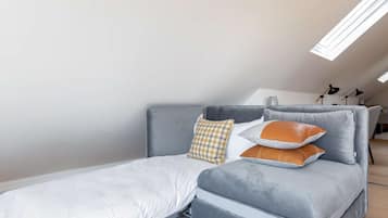 A modern loft bedroom with a grey sofa bed, a white mattress, and a checkered pillow.