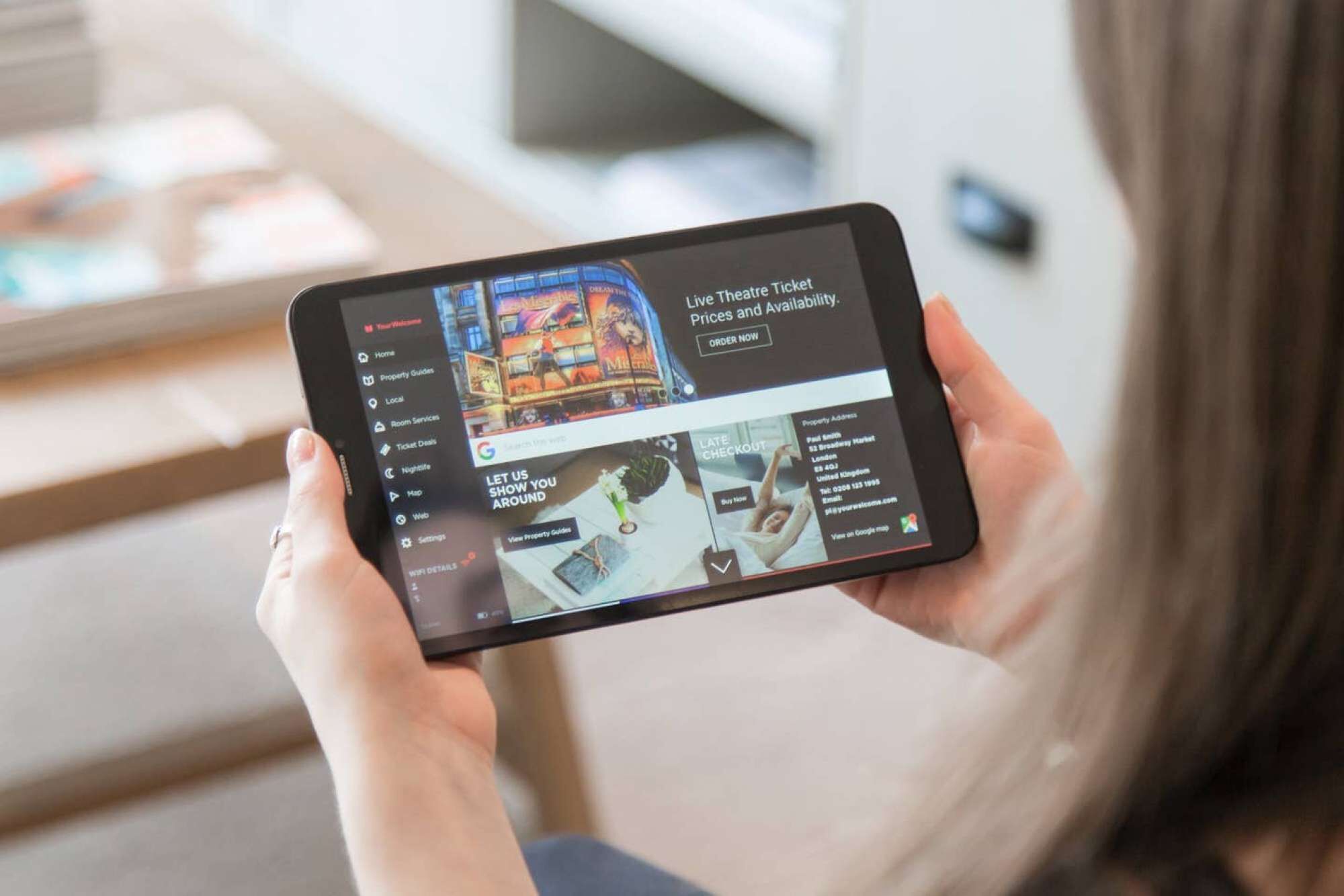 Une tablette affichant une interface de réservation de billets de théâtre en temps réel, avec des options pour les services à domicile, les événements locaux, les services en chambre et les offres spéciales sur les billets.