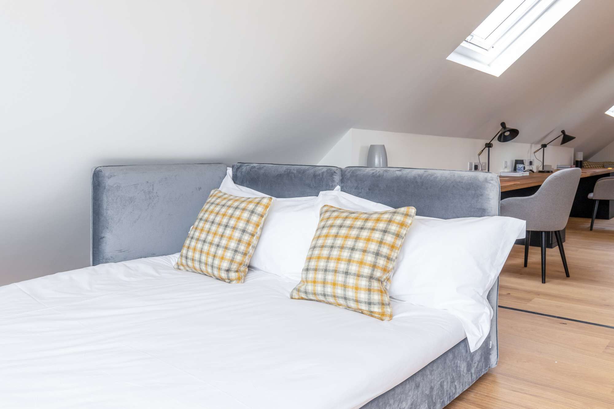 Een moderne slaapkamer met een bed, twee geruite kussens, een bureau en een stoel op de achtergrond.