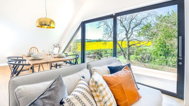 Un interior moderno con comedor, ventanas amplias y un sofá con cojines.
