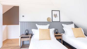 A hotel room with two single beds, a grey headboard, a small table with a lamp, and a framed picture on the wall.