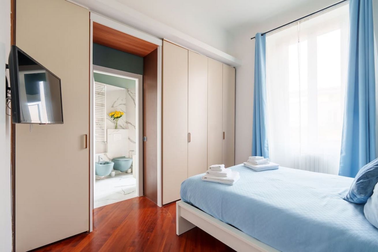 A bedroom with a bed, a wardrobe, and a bathroom visible through an open door.