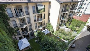 Um edifício residencial com vários andares, varandas, um pátio e uma pequena área de jardim.