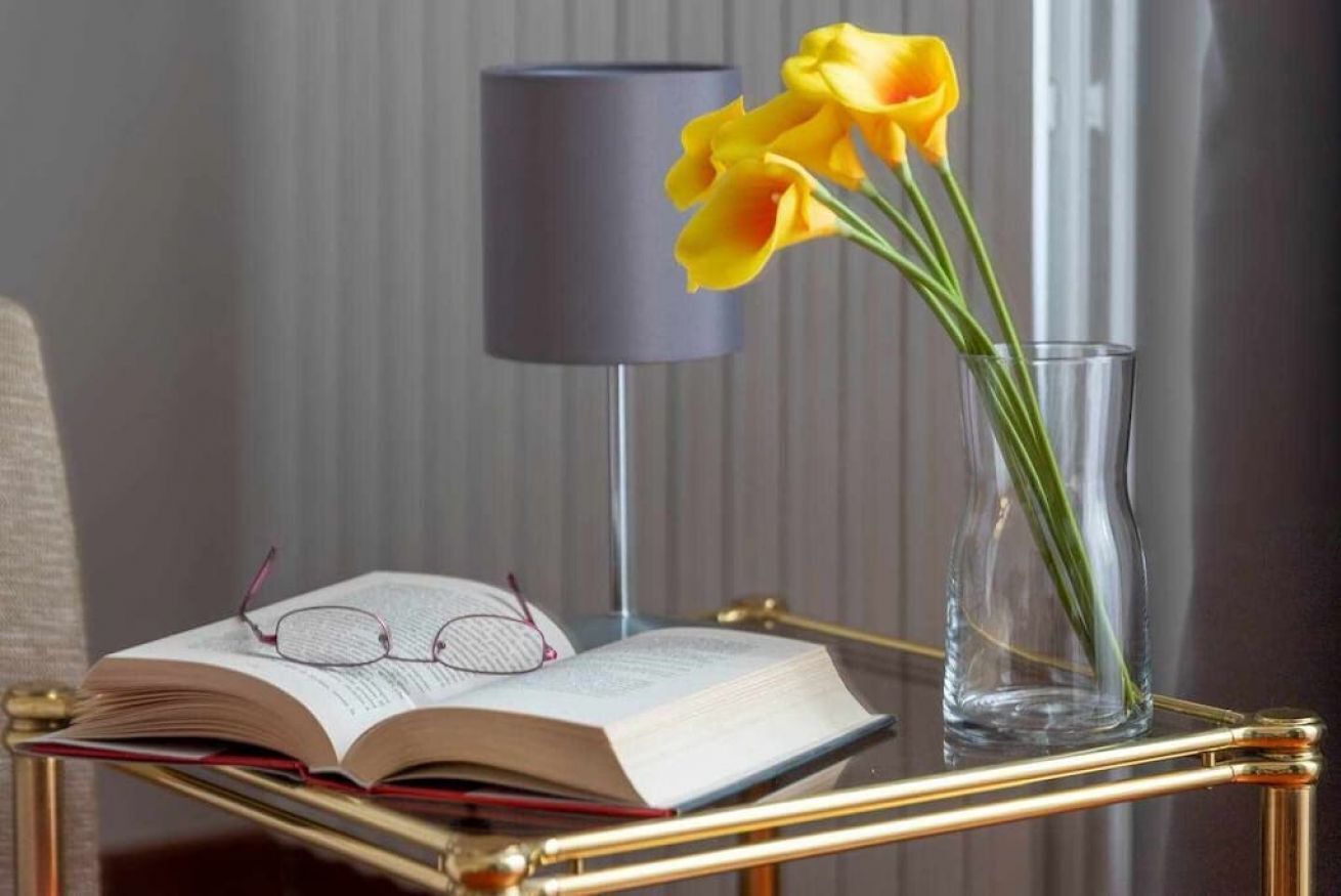 Un livre, des lunettes et un vase avec des fleurs sur une table.