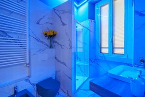 A modern bathroom with a marble wall, a black toilet, a glass shower enclosure, and a sink with a mirror.