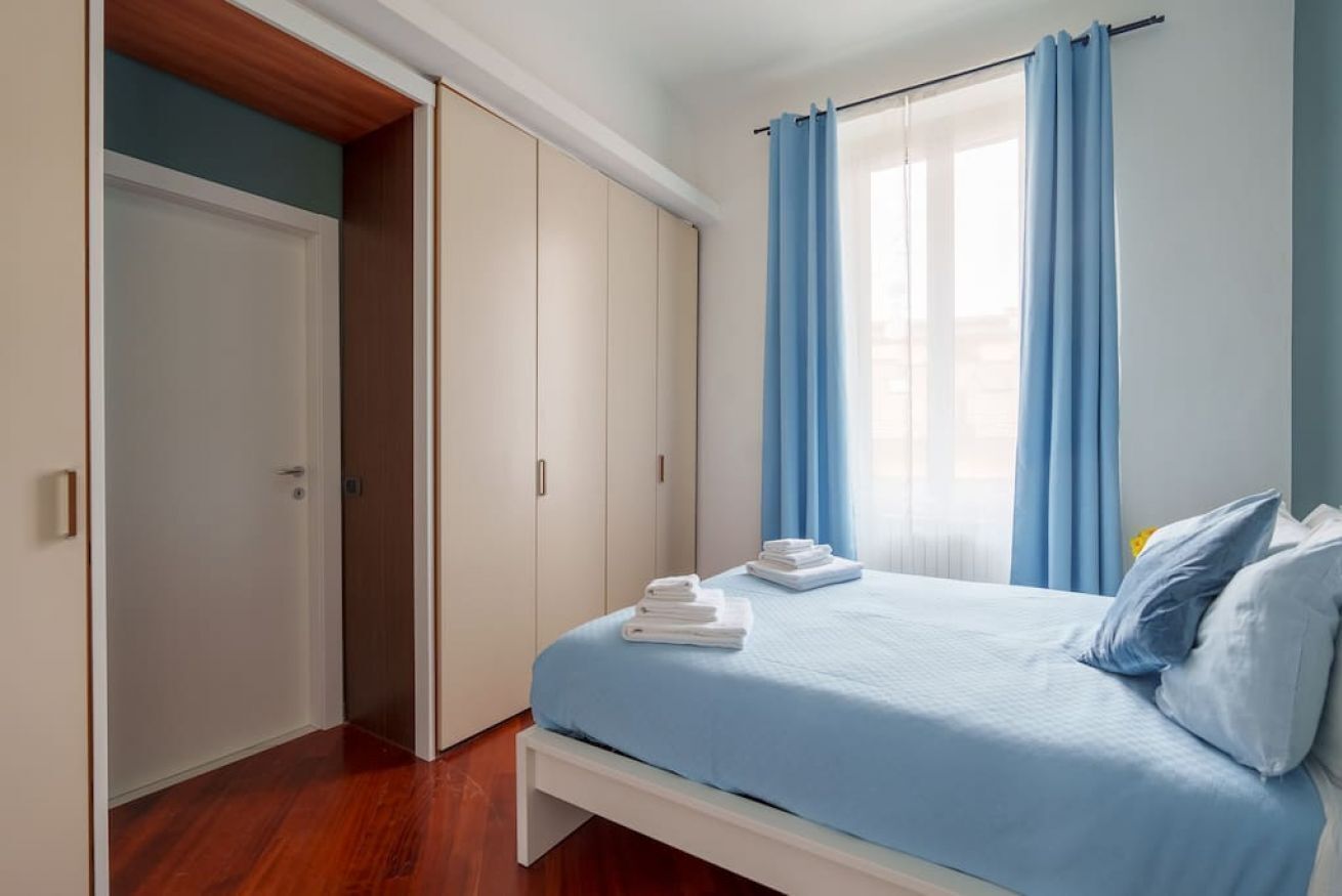 Een slaapkamer met een bed, een kledingkast en een raam met gordijnen.