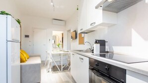 Una cocina moderna con armarios blancos, horno integrado y comedor con mesa y sillas blancas.