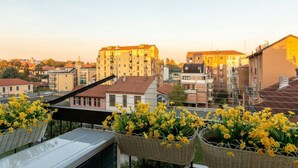 Un balcón con cestas de mimbre llenas de flores amarillas, vista de un paisaje urbano con edificios y cielo despejado.