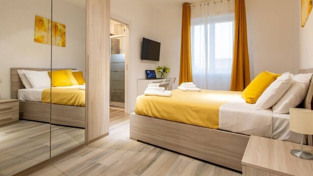 Una habitación de hotel moderna con dos camas, un espejo grande, un televisor de pantalla plana y una ventana con cortinas.