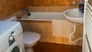 Een badkamer met een wasmachine, twee toiletten, een bad en een wastafel.