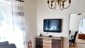Een woonkamer met een bank, salontafel, televisie, houten kast en een kroonluchter.