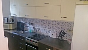 Een keuken met witte kastjes, een magnetron, een koffiezetapparaat, een waterkoker, een spoelbak en een fornuis.