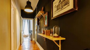A hallway with wooden flooring, a pendant light, a shelf with decorative items, and a framed picture on the wall. - The Palm Leaf SOC in Lisboa Ciudad (Lisbon)