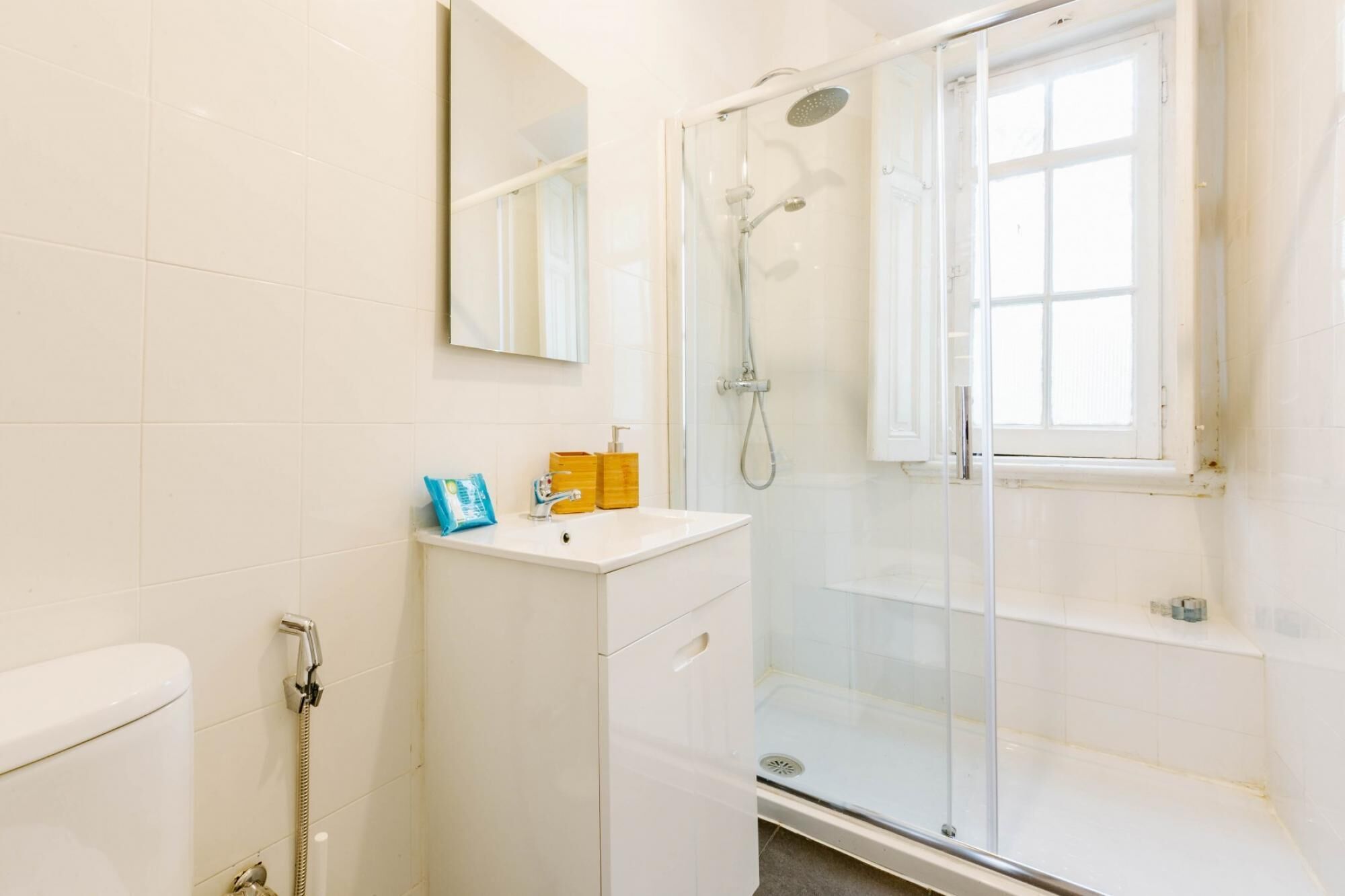 A modern bathroom with a glass-enclosed shower, a white sink with toiletries, and a large mirror.