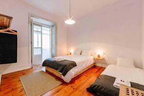 A bedroom with a wooden bed, a bedside table with a lamp, a window, and a hanging garment rack. - The Palm Leaf SOC in Lisboa Ciudad (Lisbon)