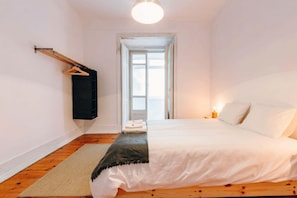 A bedroom with a bed, a hanging clothes rack, a door leading outside, and a small bedside table with a lamp. - The Palm Leaf SOC in Lisboa Ciudad (Lisbon)