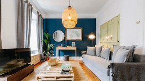 A living room with a TV, a sofa, a coffee table, and a hanging light fixture. - The Palm Leaf SOC in Lisboa Ciudad (Lisbon)