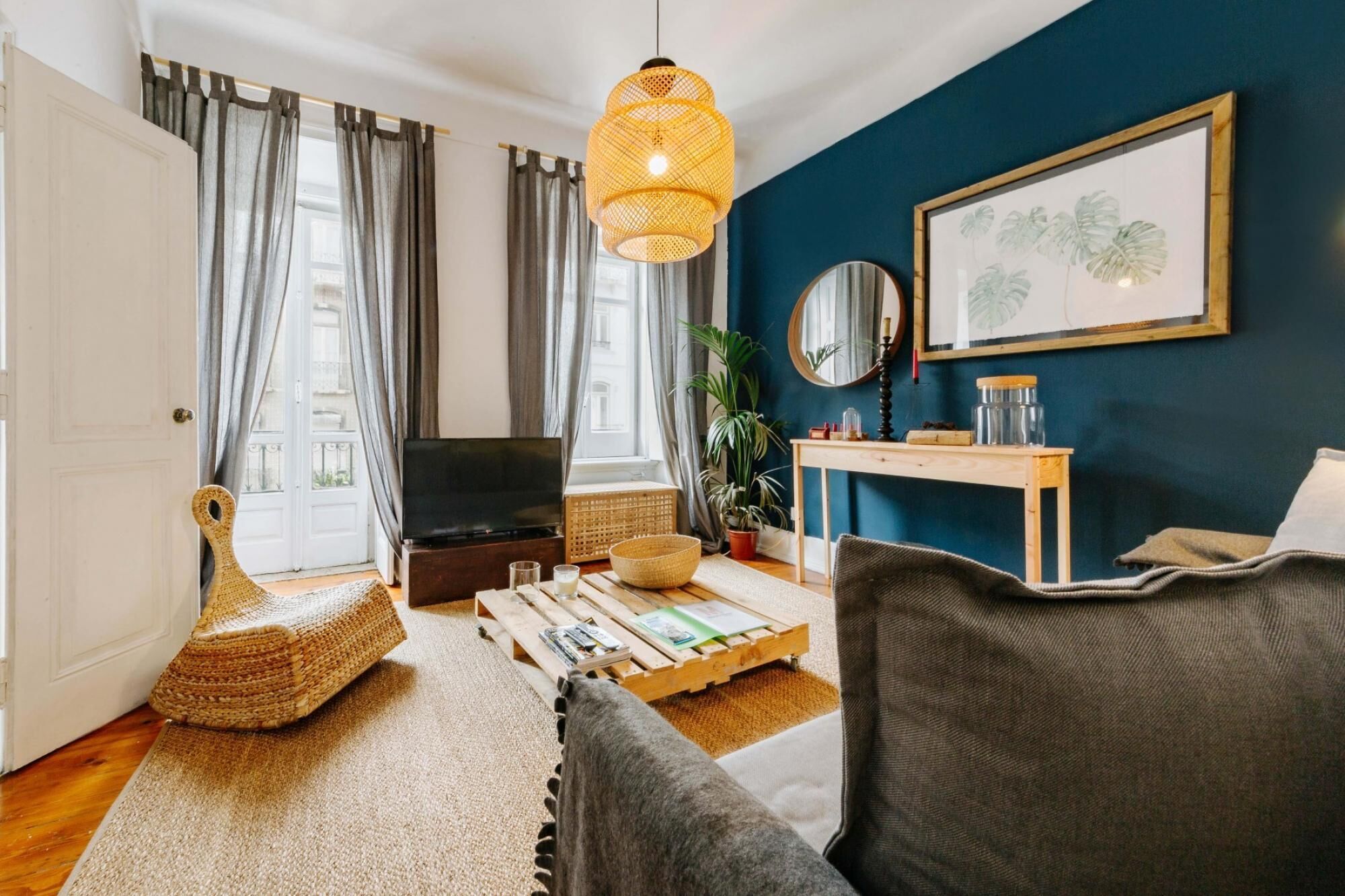 Un salon chaleureux avec un téléviseur, un fauteuil en osier, une table basse en bois et un mur d’accent bleu.