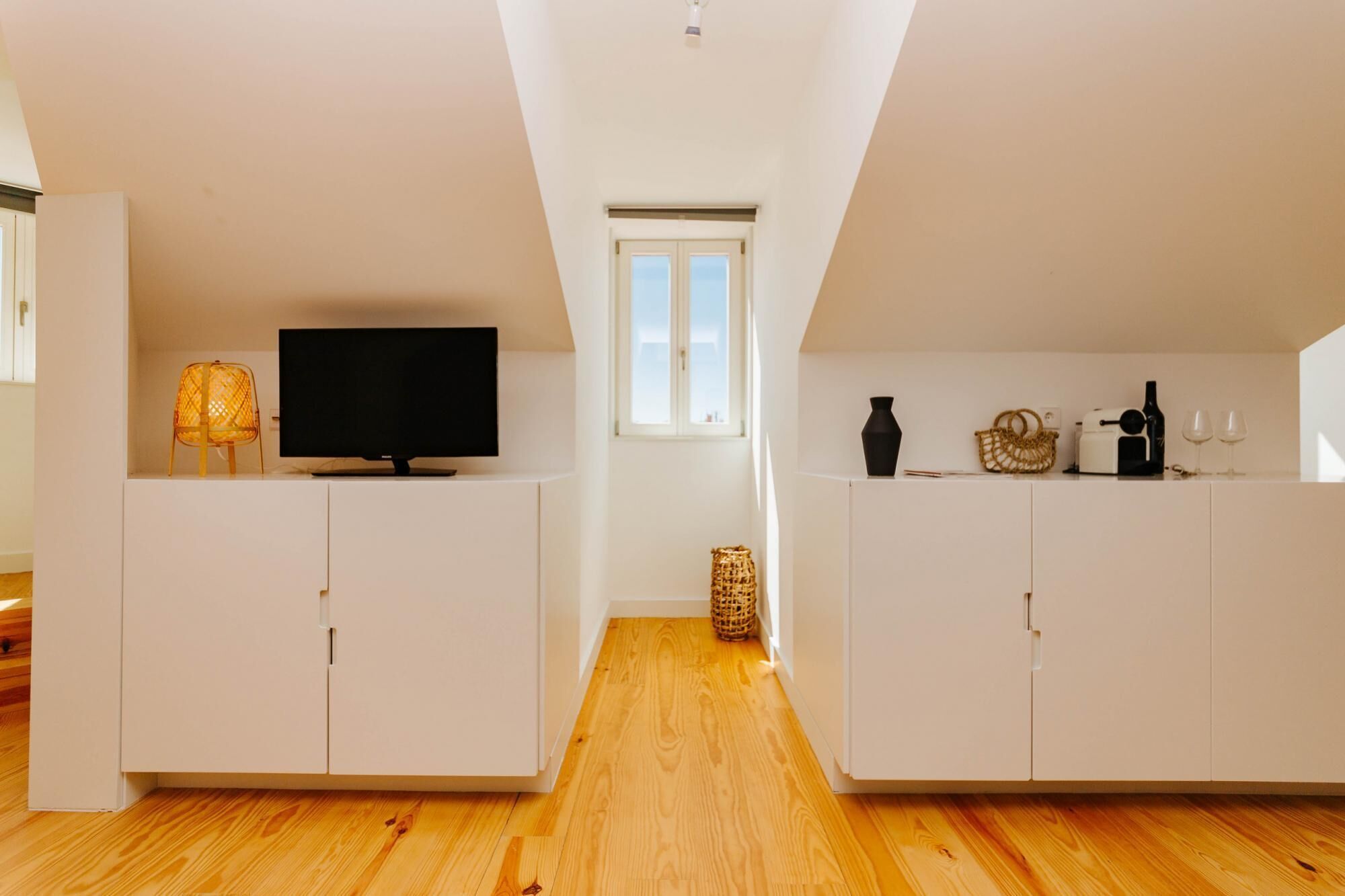Eine moderne Wohnung mit Fernseher auf einem Schrank, Holzboden, weißen Schränken, einem kleinen Fenster und einem Korb auf dem Boden.