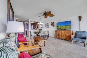A living room with a wooden coffee table, a sofa with patterned cushions, a television, and a ceiling fan.