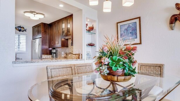A modern kitchen with wooden cabinets, a built-in oven, and a dining area with a glass table and wicker chairs.