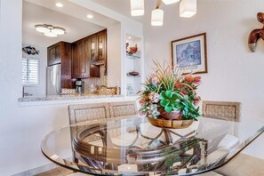 A modern kitchen with wooden cabinets, a built-in oven, and a dining area with a glass table and wicker chairs.
