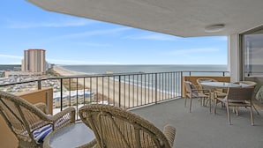 En balkon med fletningsmøbler, udsigt til stranden og en høj bygning i det fjerne.