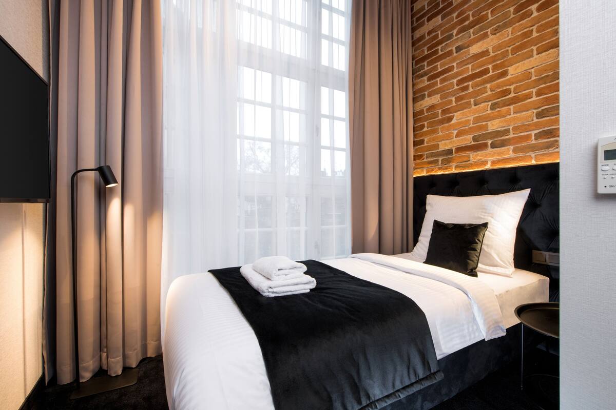 A hotel room with a bed, a black headboard, a wall clock, and a window with curtains.