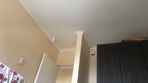 Ett rum med ett vitt tak, en synlig lampa, en vit vägg med ett eluttag och en mörkfärgad dörr.
